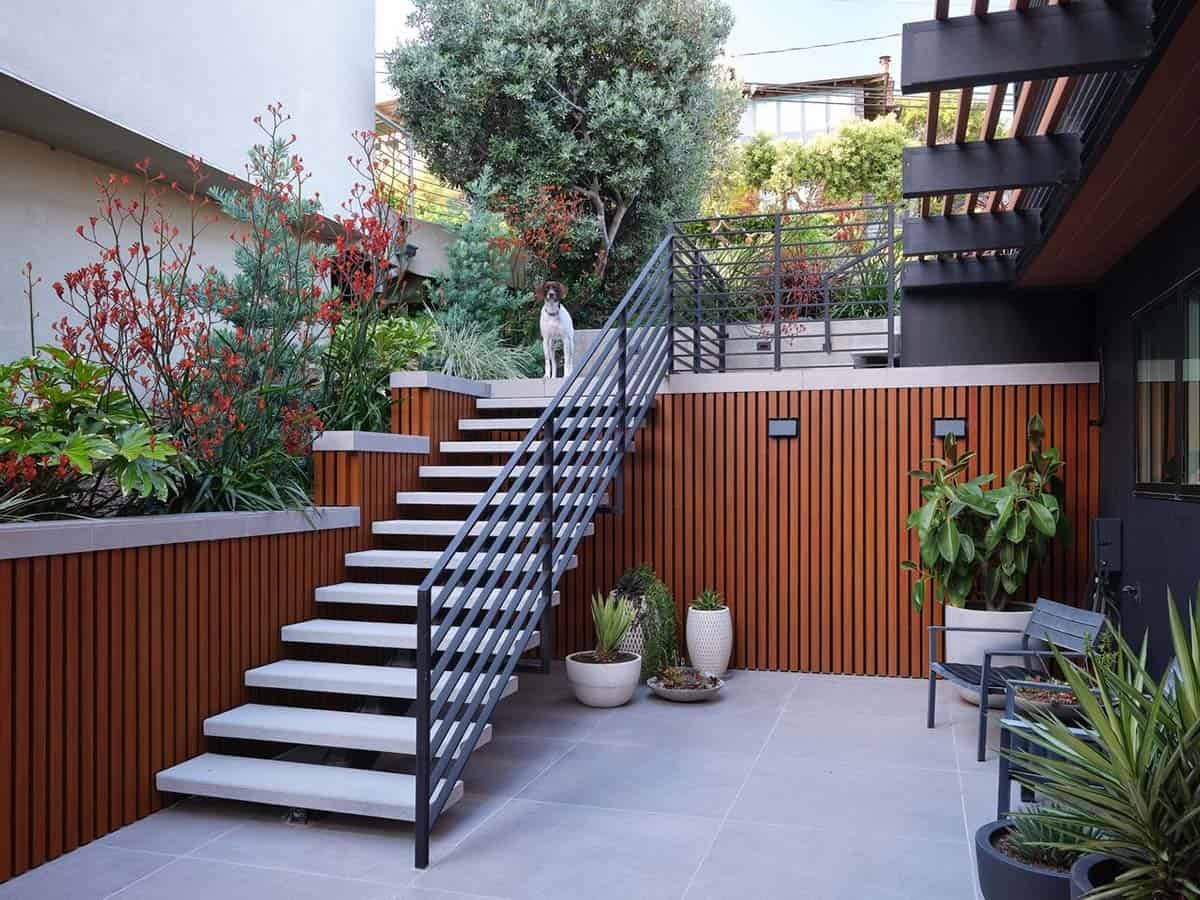 midcentury modern hillside home outdoor courtyard with floating stairs black railing cedar slat retaining wall and family dog Point Richmond