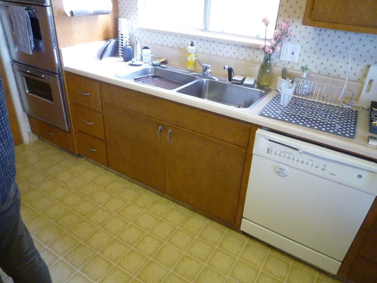 before renovation original midcentury kitchen with wood cabinets yellow vinyl floor and dated wallpaper Point Richmond California