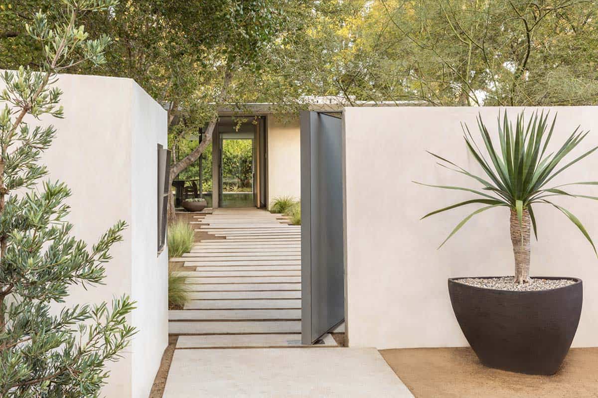 White stucco gate wall with pivot door and potted yucca plant