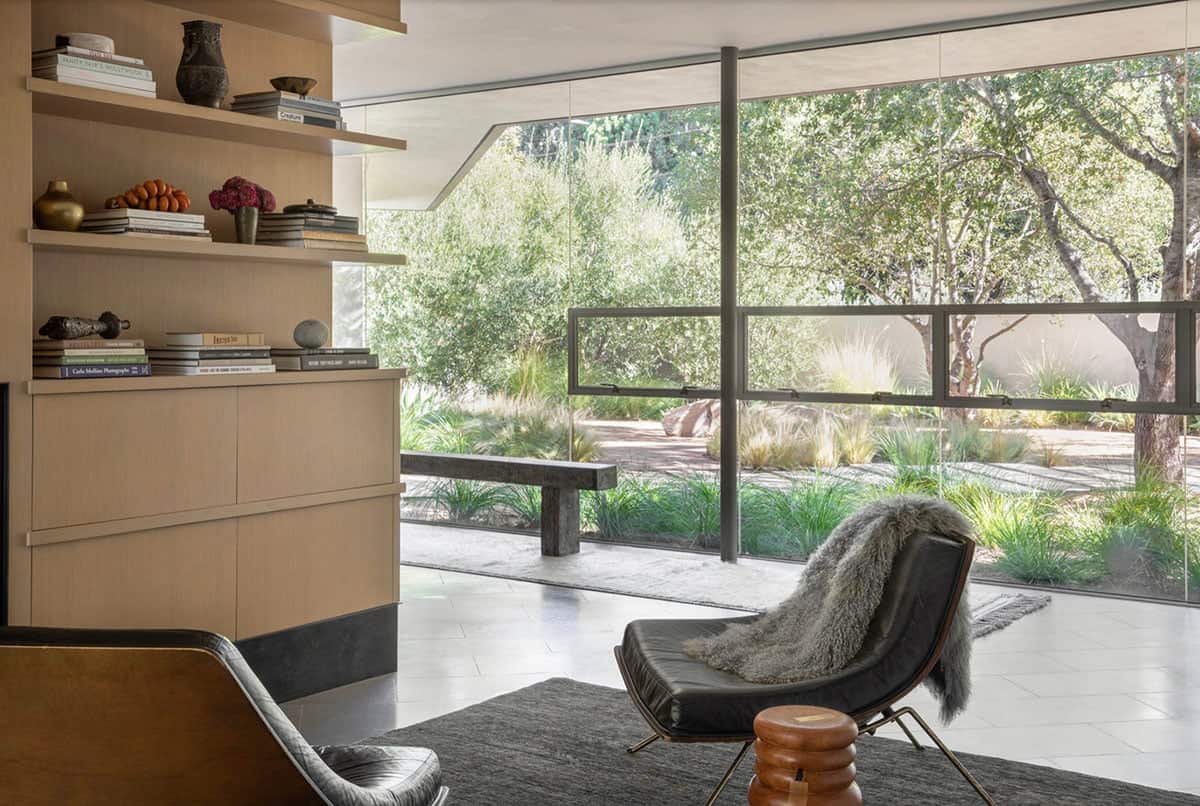 Living room corner with leather lounge chair facing floor-to-ceiling garden windows