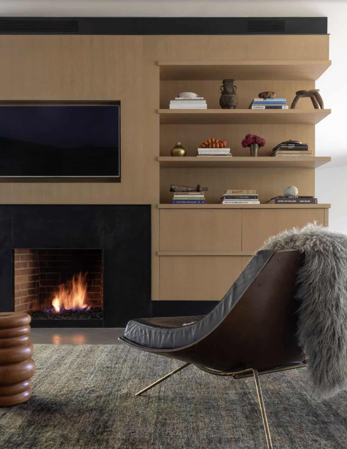 Warm oak fireplace wall with built-in shelving and leather lounge chair
