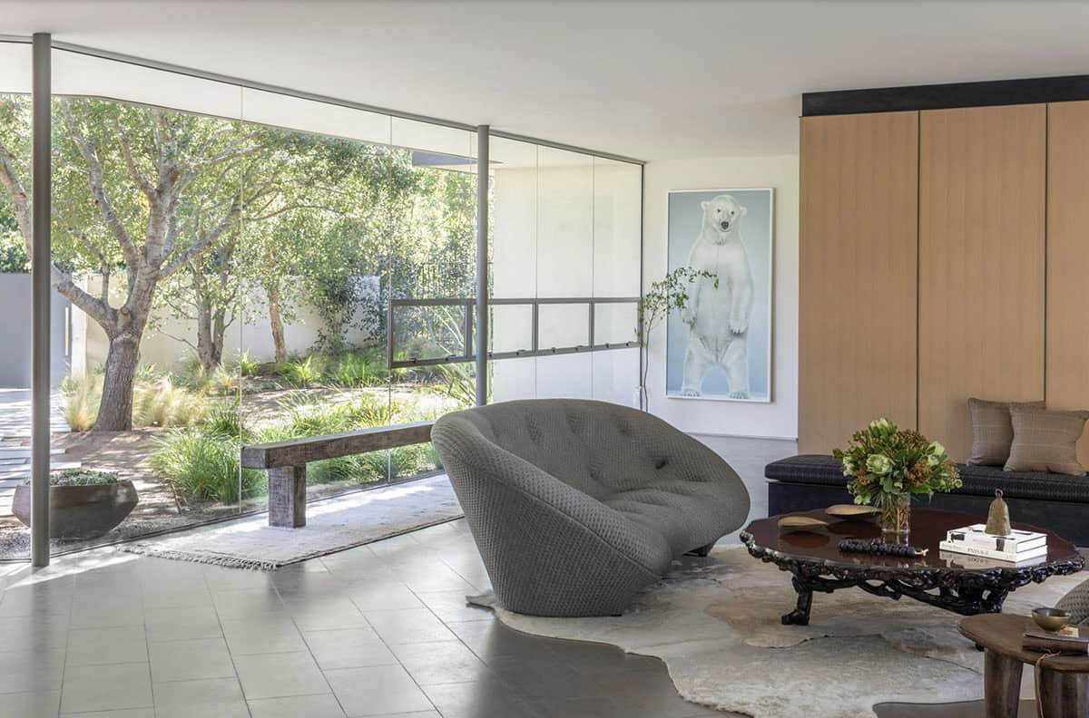 Living room with gray tufted sofa, ornate coffee table, and glass walls