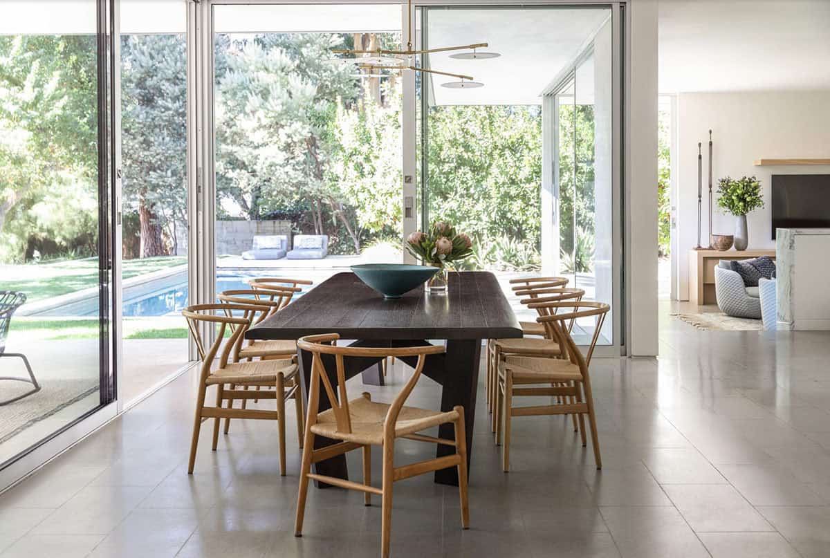 Dark wood dining table with wishbone chairs overlooking backyard pool area