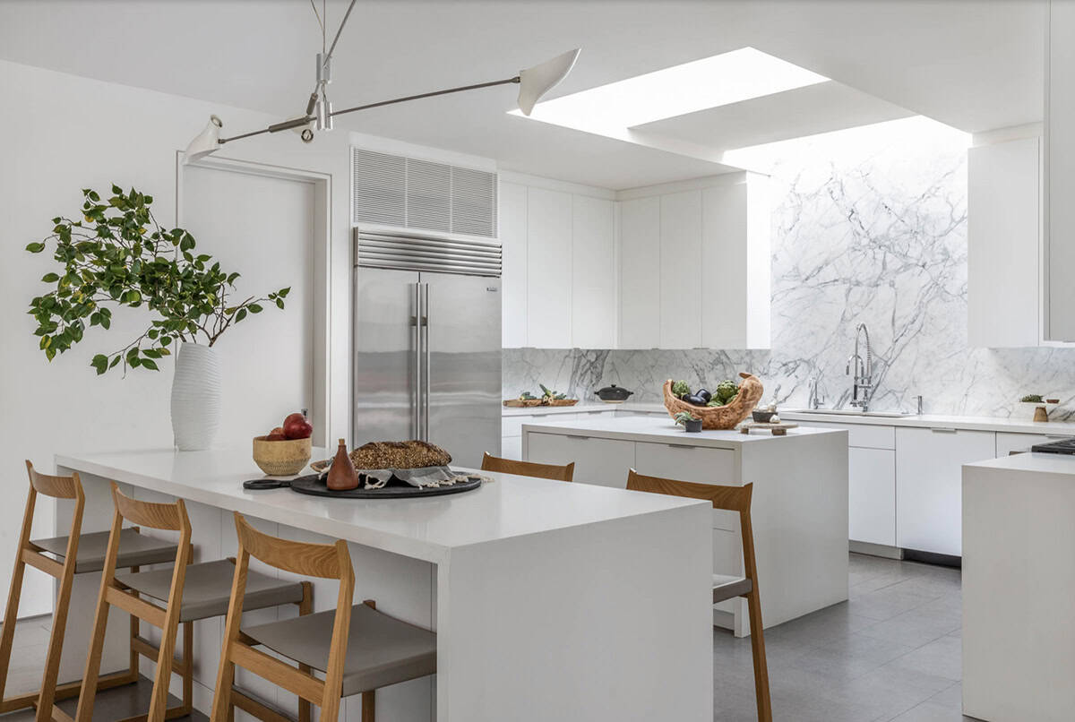 All-white kitchen with marble backsplash, dual islands, and overhead skylight