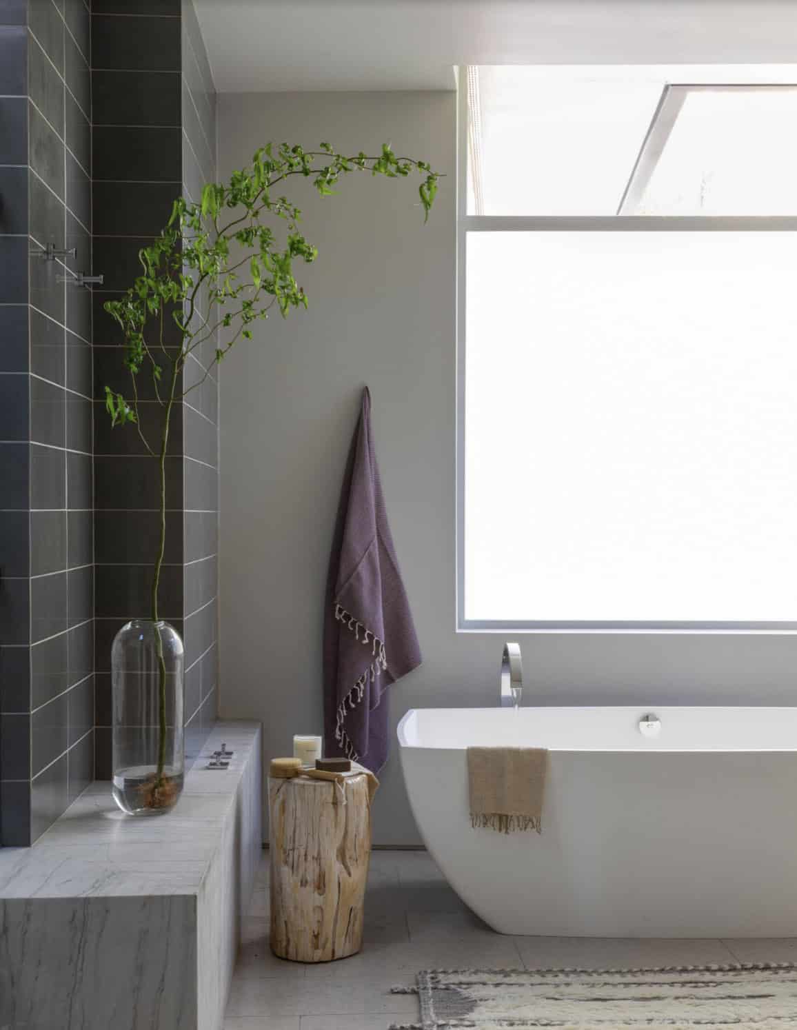 Freestanding soaking tub beside skylight window with dark tile shower wall