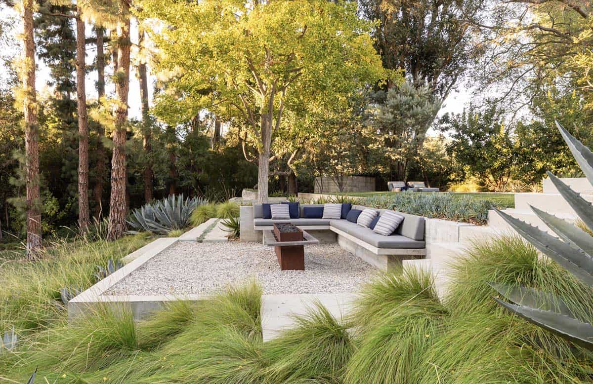 Sunken gravel fire pit lounge with concrete built-in seating amid ornamental grasses