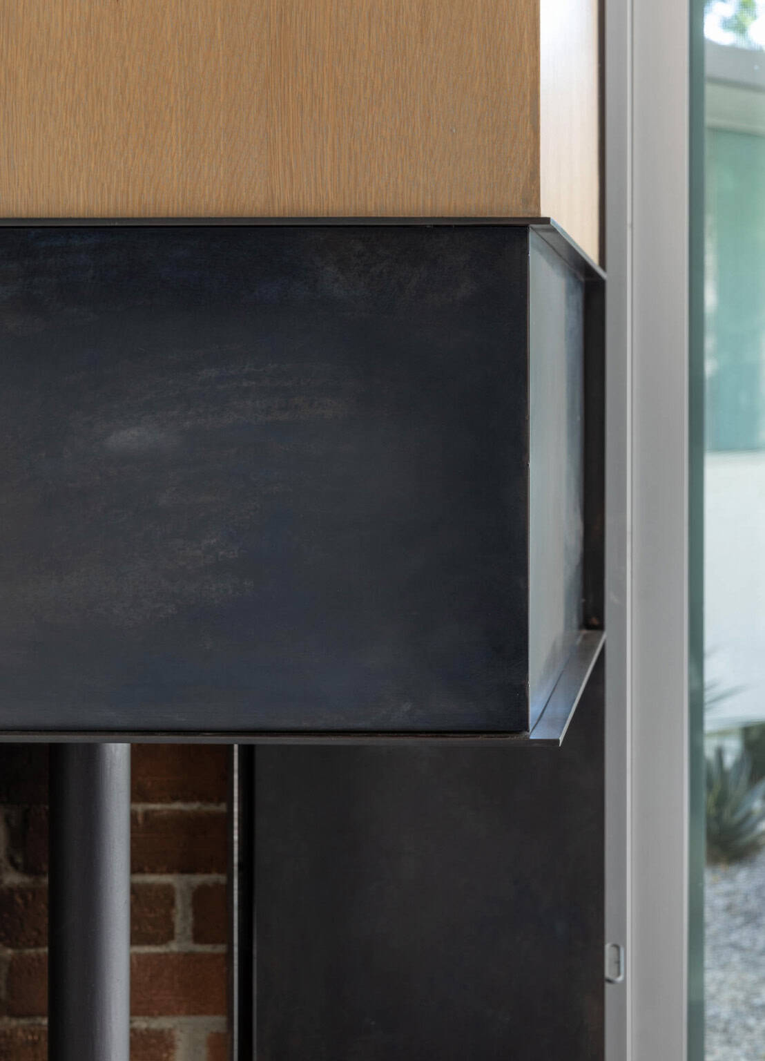Close-up detail of blackened steel fireplace surround meeting oak wood paneling