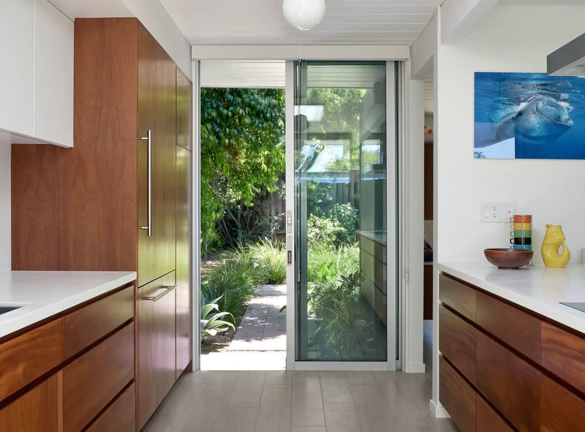 mid-century modern kitchen galley with walnut cabinets white countertops sliding glass door and underwater photography wall art