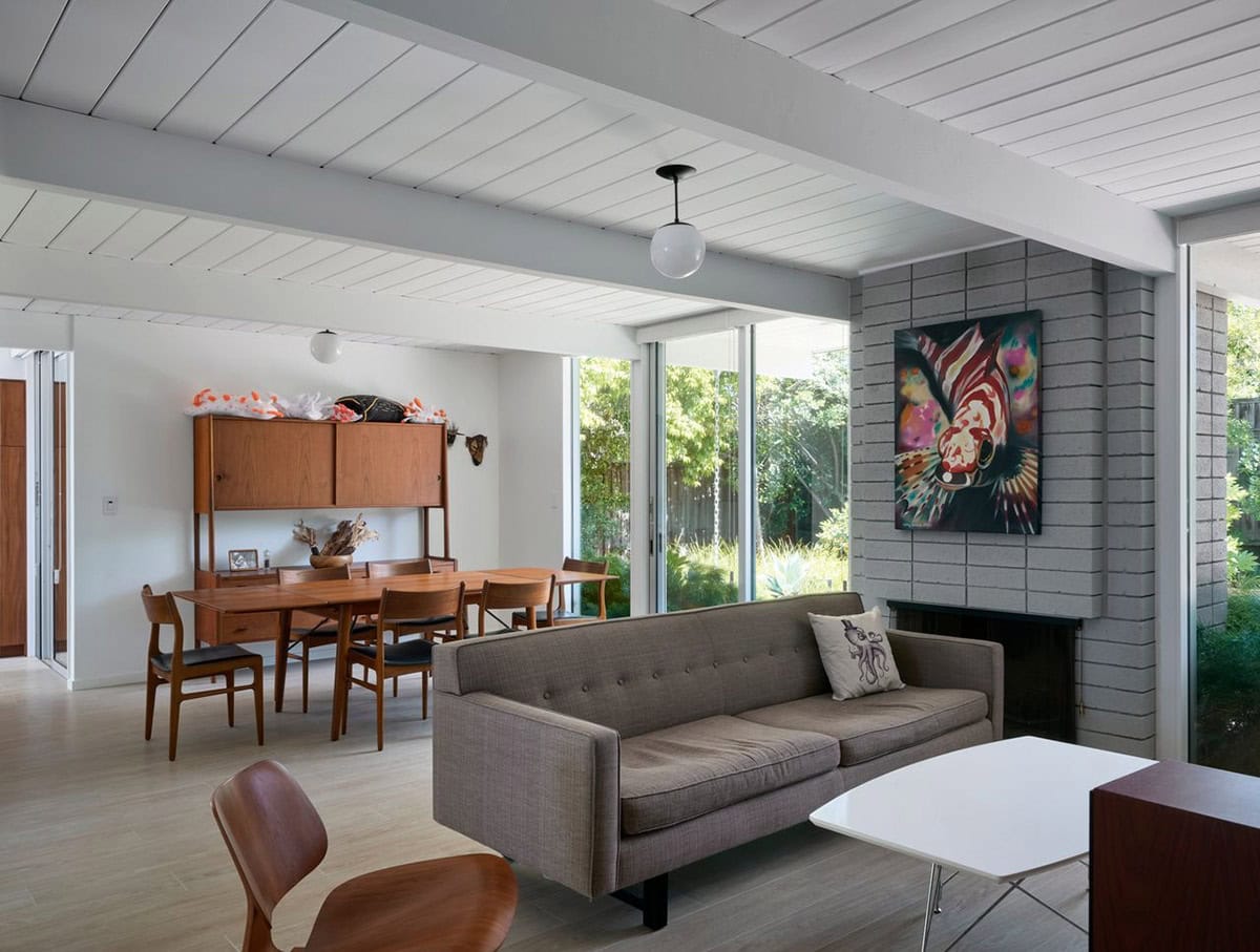 open plan mid-century modern living and dining room with teak furniture gray brick fireplace and sliding glass doors to garden