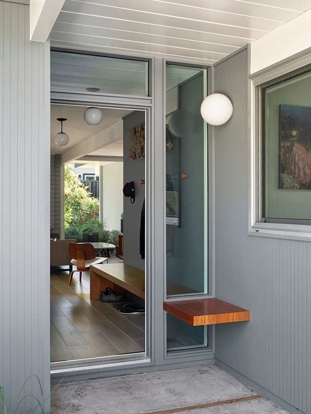 Eichler home exterior entry with gray siding sliding glass door walnut floating bench and globe wall sconce Sunnyvale California