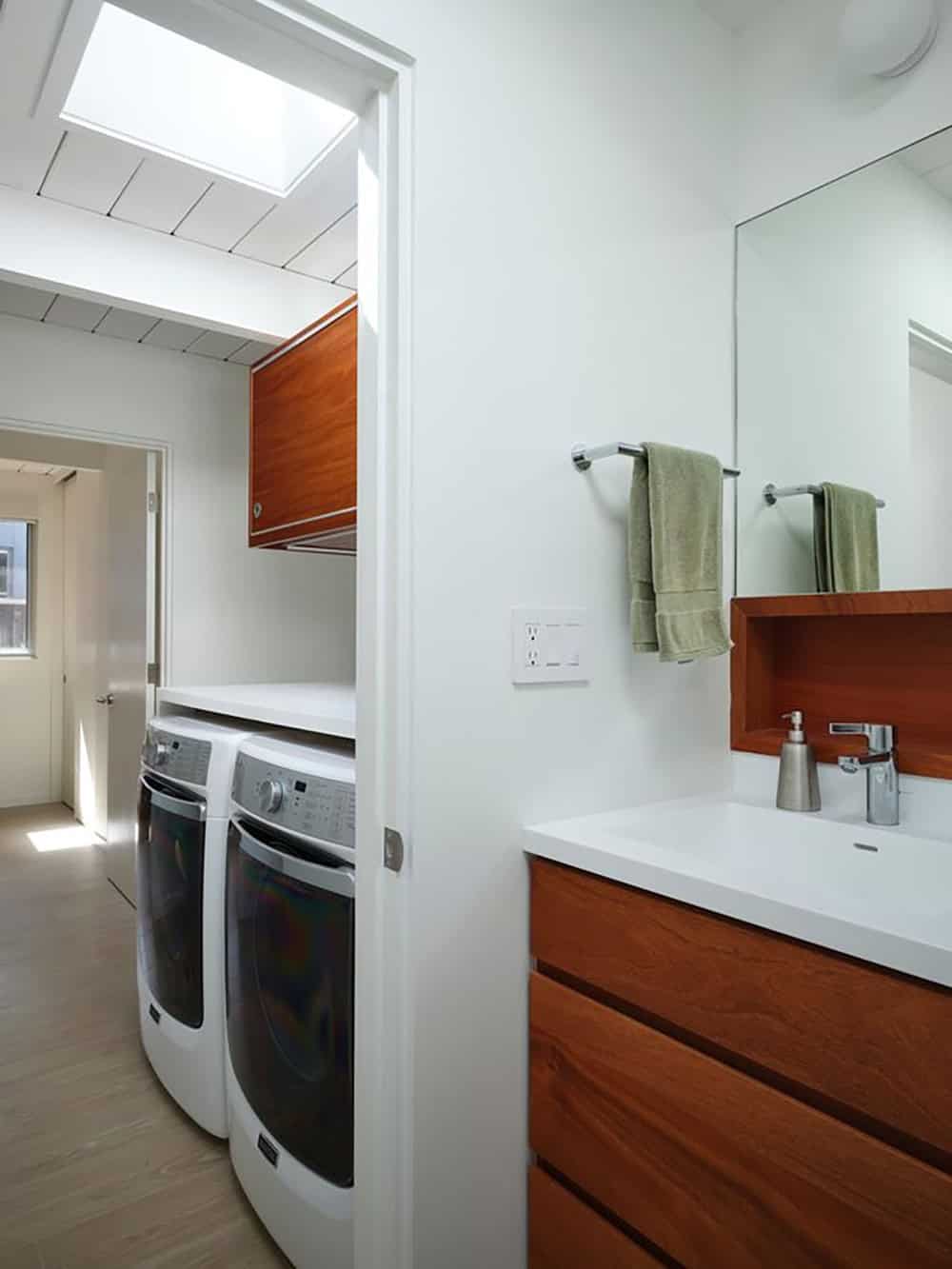 mid-century modern bathroom and laundry room with walnut cabinetry skylight side by side washer dryer and white countertop
