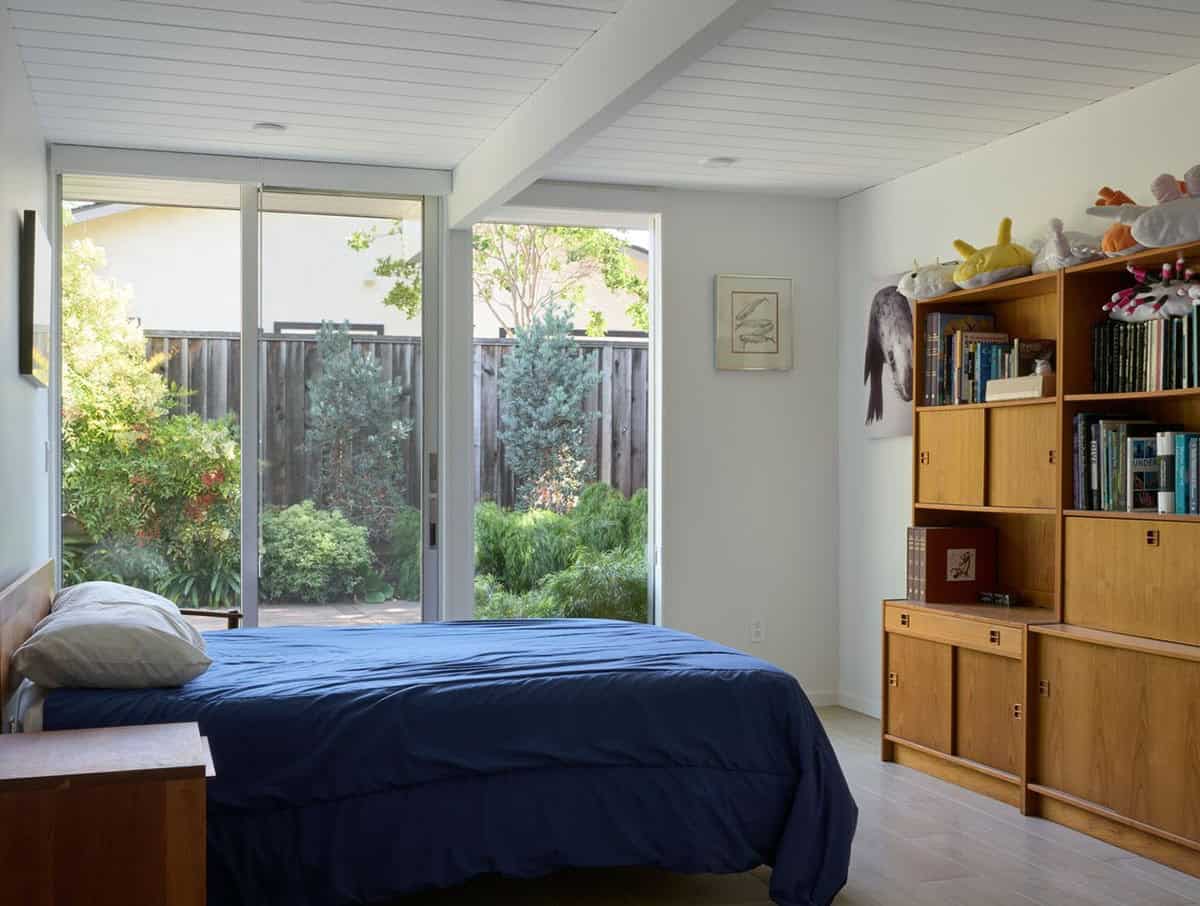 mid-century modern bedroom with navy bedding teak bookcase shelving and sliding glass doors opening to garden