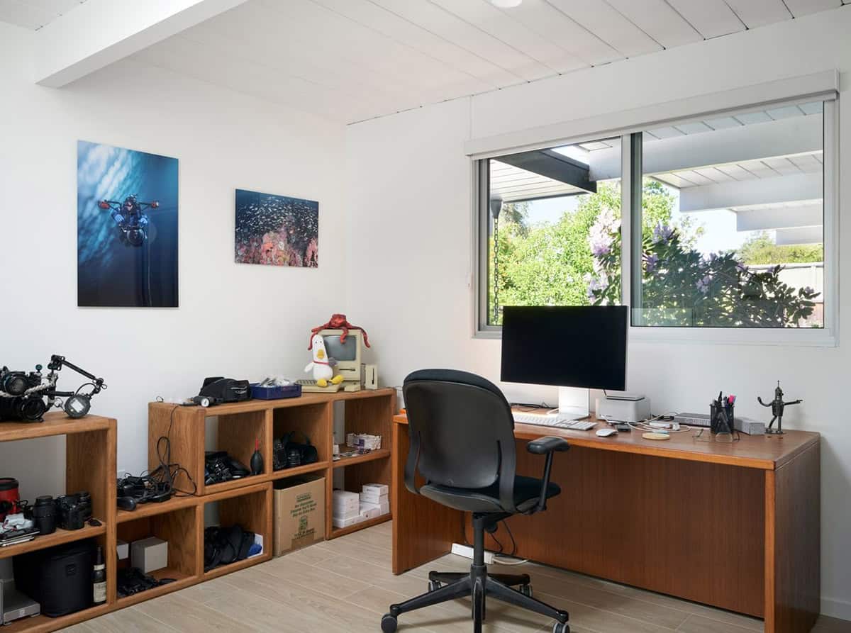 home office with underwater photography wall art camera equipment open teak shelving and garden view Eichler renovation