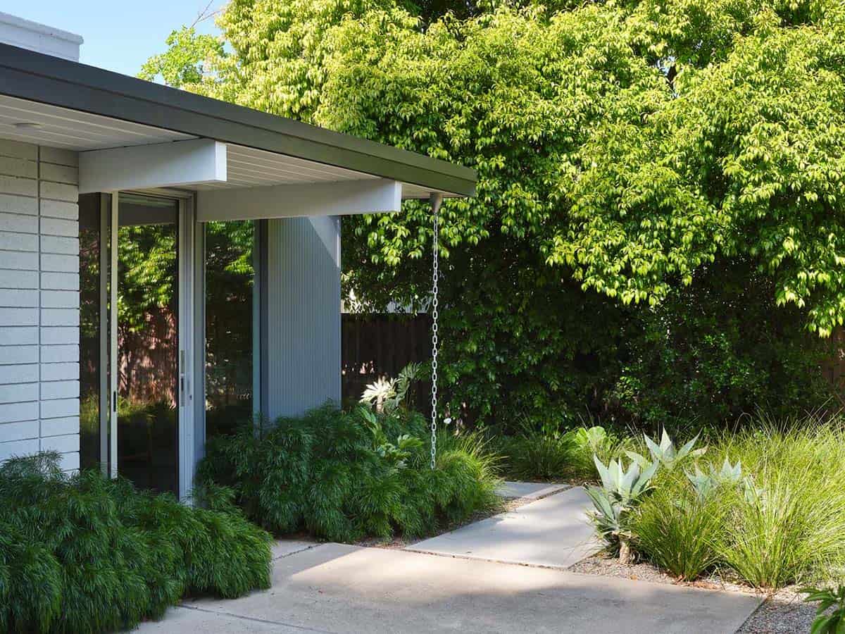 renovated Eichler home exterior with flat roof overhang rain chain drought tolerant landscaping and sliding glass doors