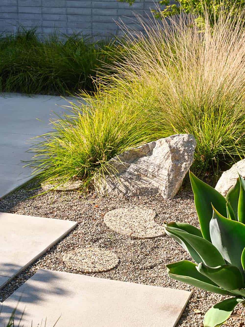 drought tolerant front garden with ornamental grasses agave boulders gravel and concrete stepping stones mid-century modern home