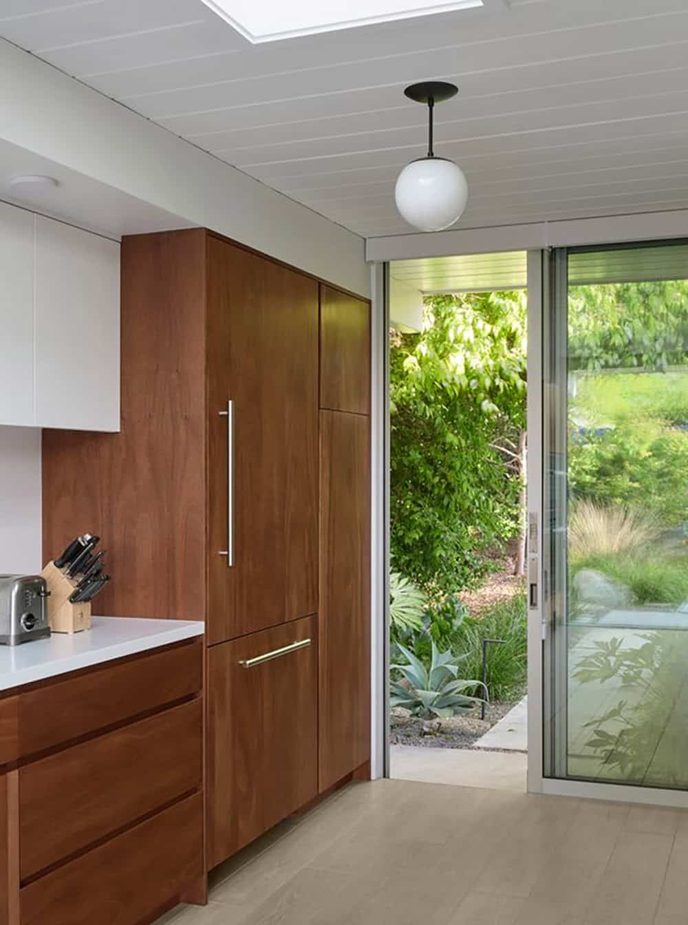 renovated Eichler kitchen with panel ready refrigerator walnut cabinetry skylight globe pendant and sliding door to garden