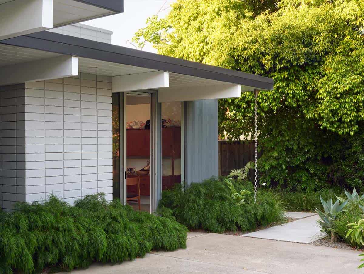 Eichler home exterior corner with concrete block wall flat roof overhang rain chain asparagus fern groundcover and garden path