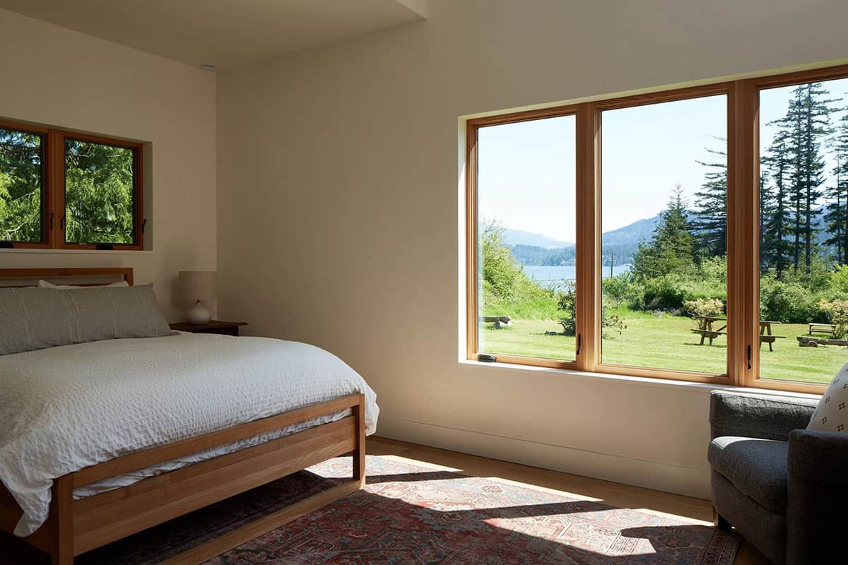 Wide view of the NorthShore Residence primary bedroom showing natural light, warm materials, and a peaceful forest outlook