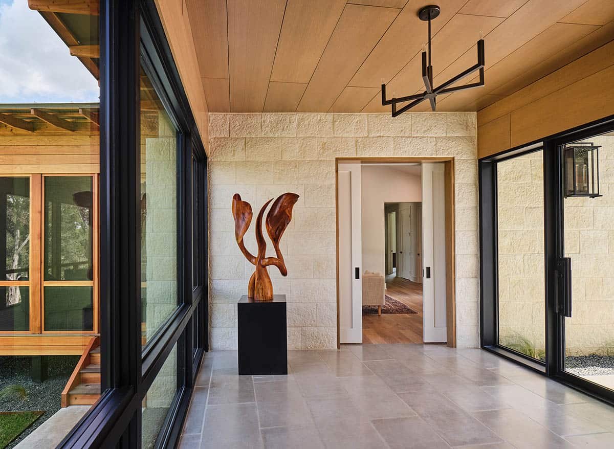 modern home entryway with a stone wall, wood ceiling, and large windows overlooking a patio