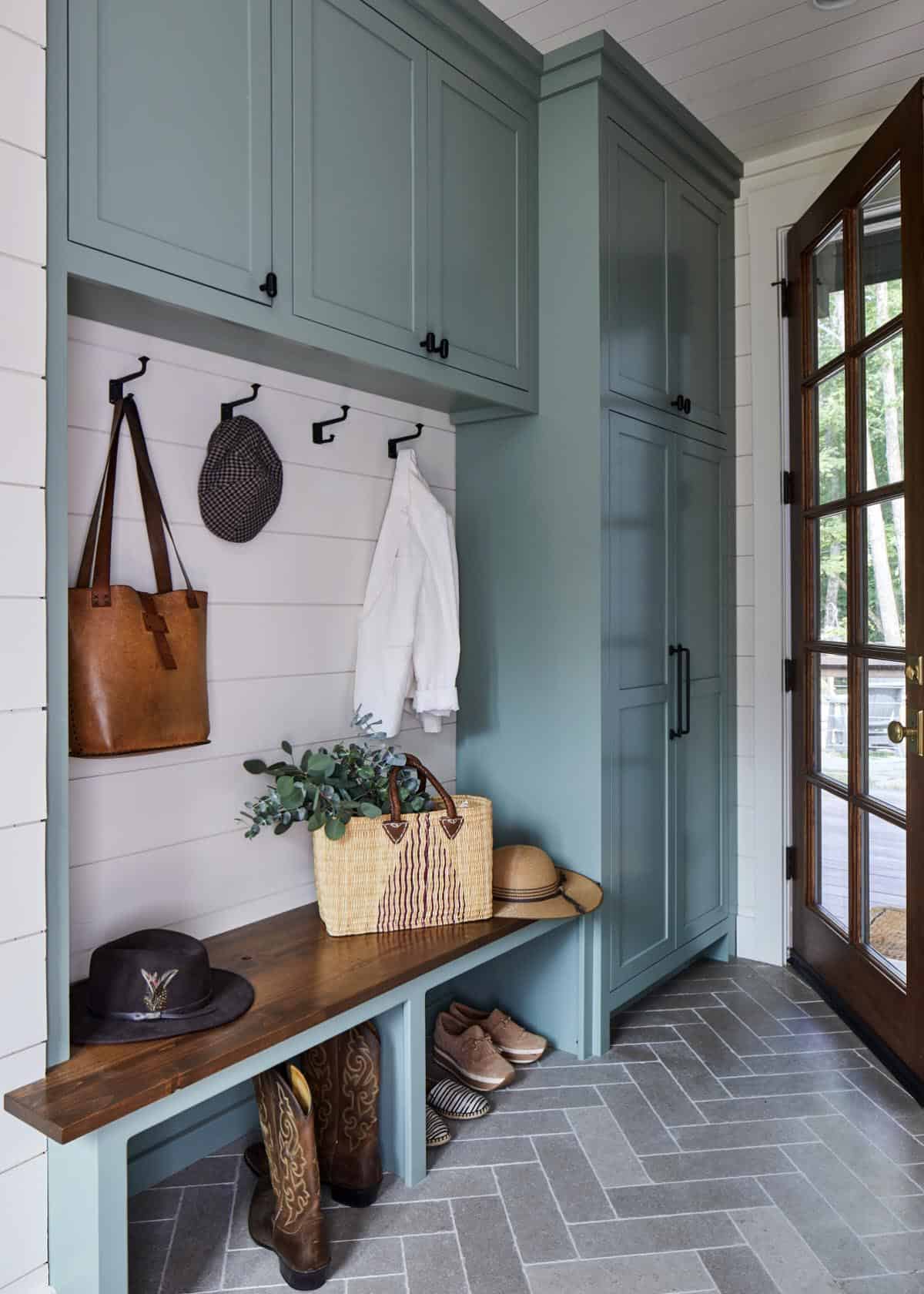 Mudroom with sage green shaker cabinets, white shiplap, walnut bench, black iron coat hooks, herringbone slate tile floor, and French door entry with wooded view