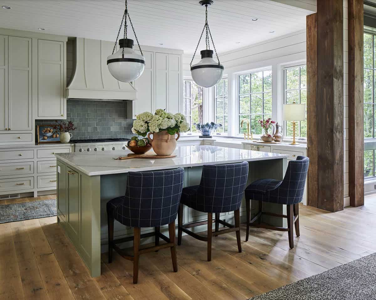 Mountain home kitchen with sage green island, navy plaid upholstered barstools, white perimeter cabinetry, custom range hood, teal subway tile backsplash, globe pendants, marble countertops, and reclaimed wood post