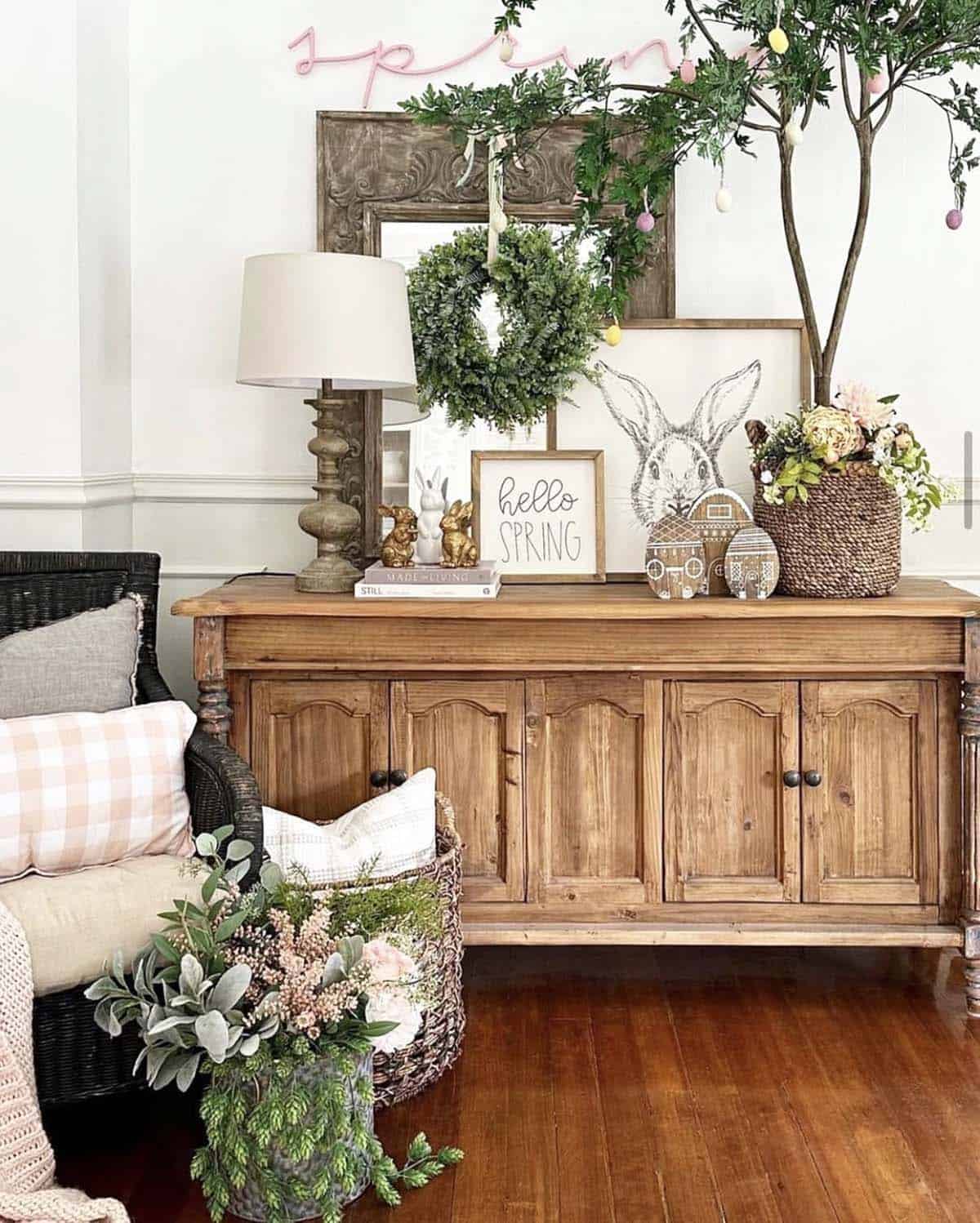 Spring console table styling with Easter bunnies, a boxwood wreath, Easter egg topiary, hello spring sign, and a wicker basket of blooms on a rustic pine sideboard