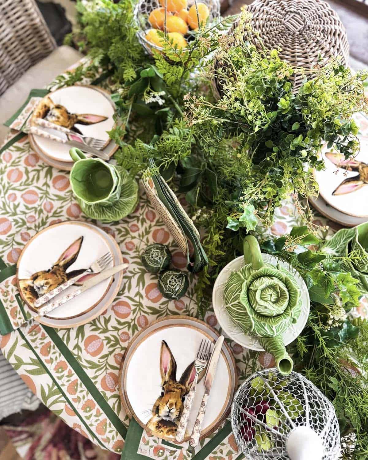Spring Easter table setting with bunny plates, cabbage teapot, lush greenery garland, and floral tablecloth