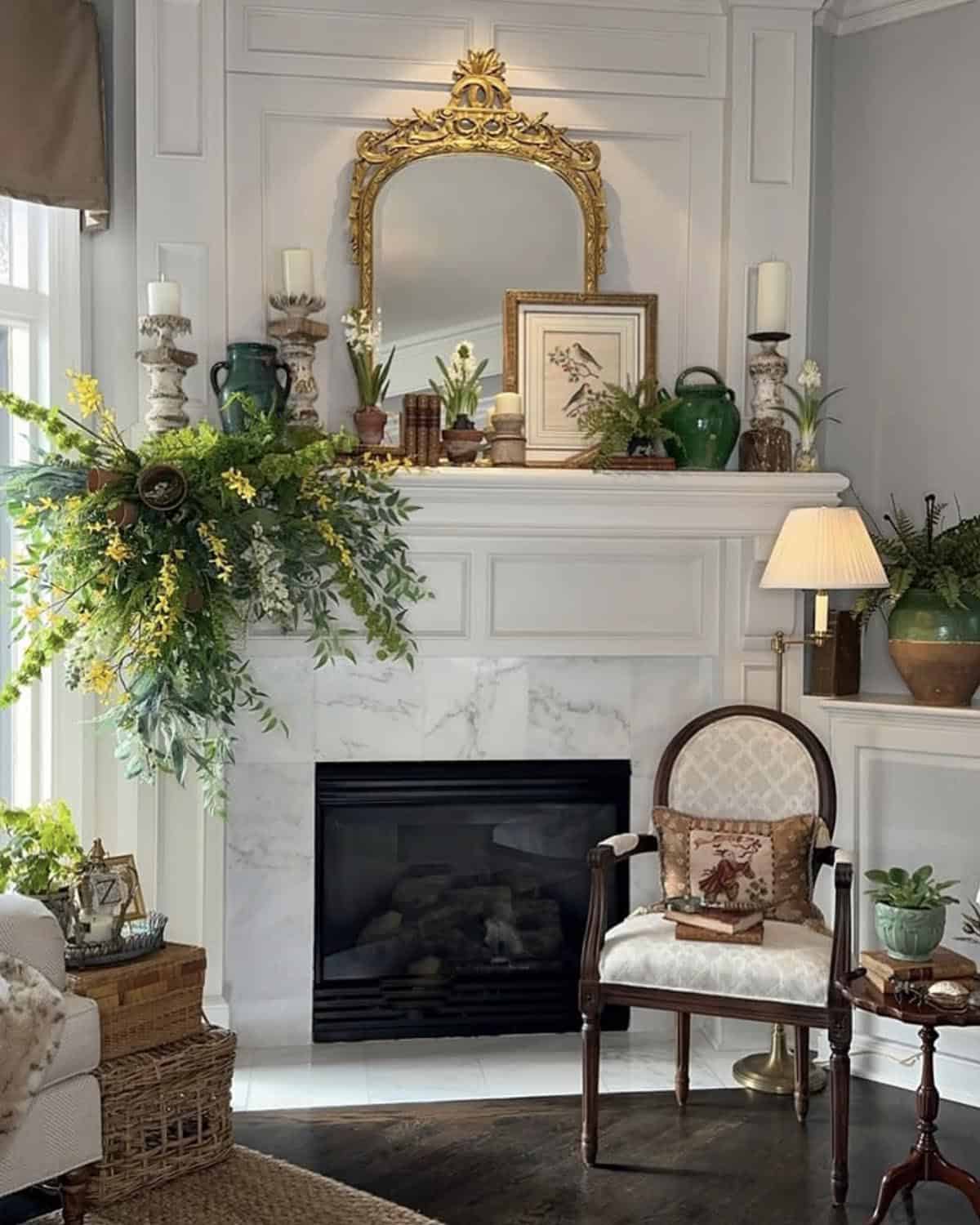 Spring fireplace mantel with cascading greenery, gold ornate mirror, botanical art, and green ginger jars