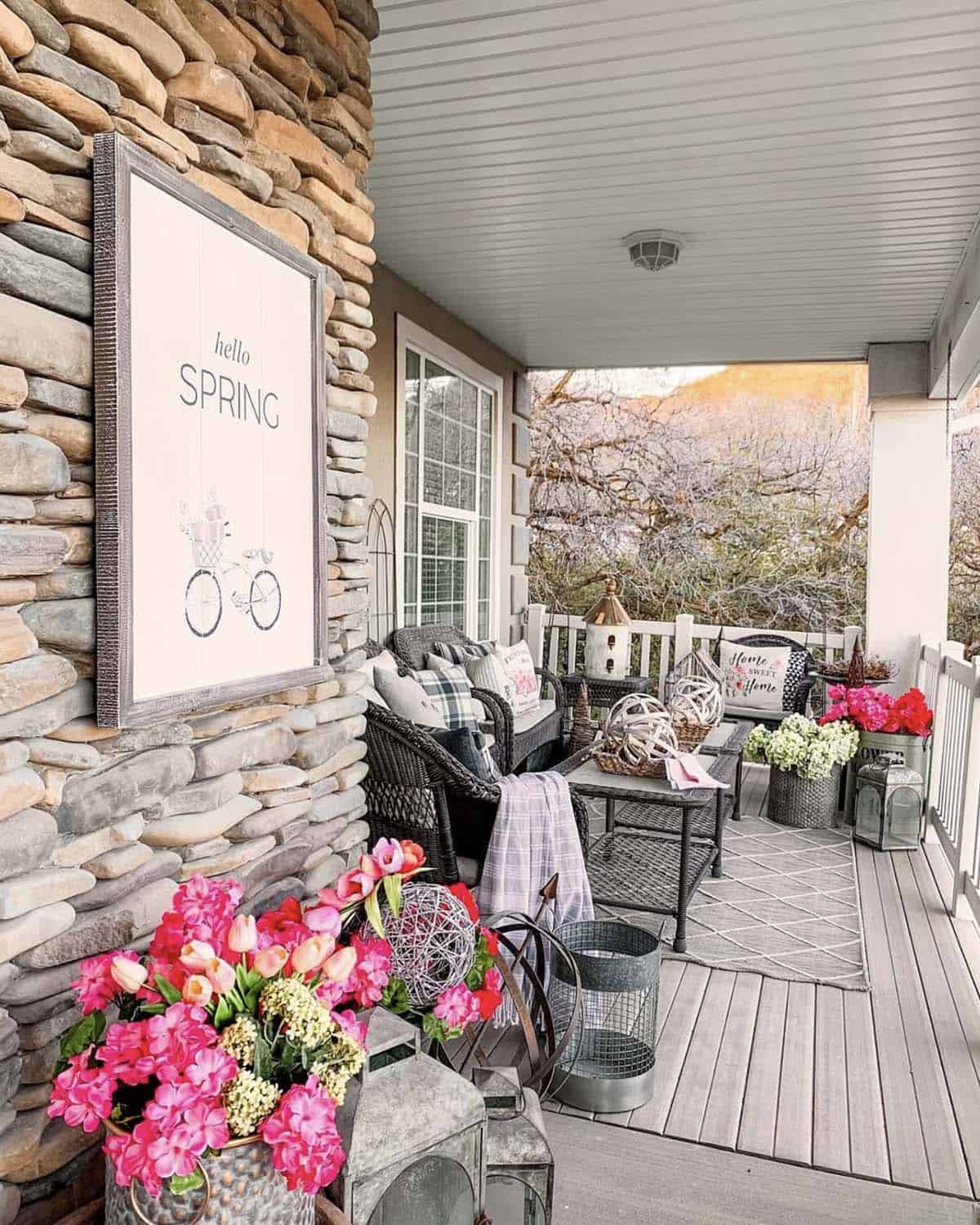 Spring front porch with bold pink florals, wicker furniture, hello spring sign, and galvanized lanterns