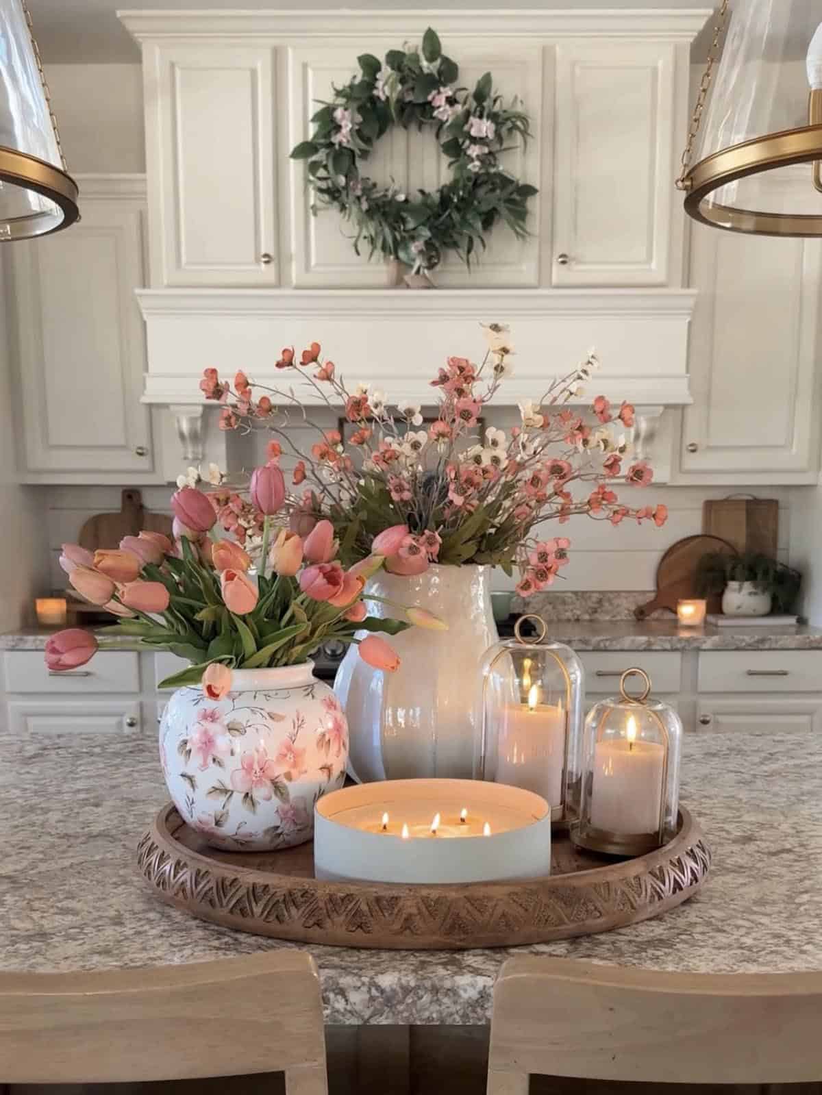 Round carved wood tray with pink tulips, floral vase, glass cloches and candles on kitchen island