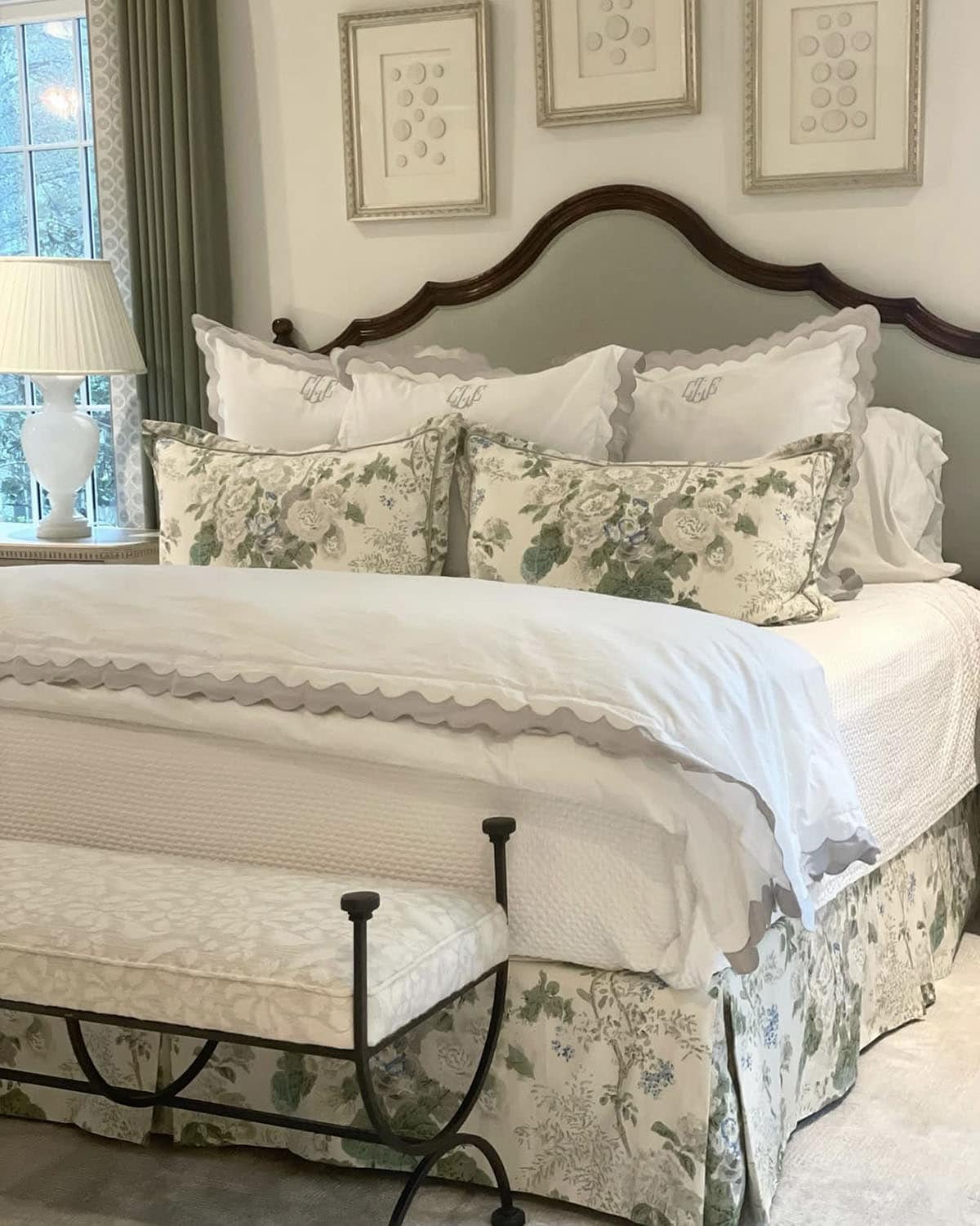 Elegant bedroom with dark wood camelback bed, monogrammed scalloped shams, and green floral bedskirt
