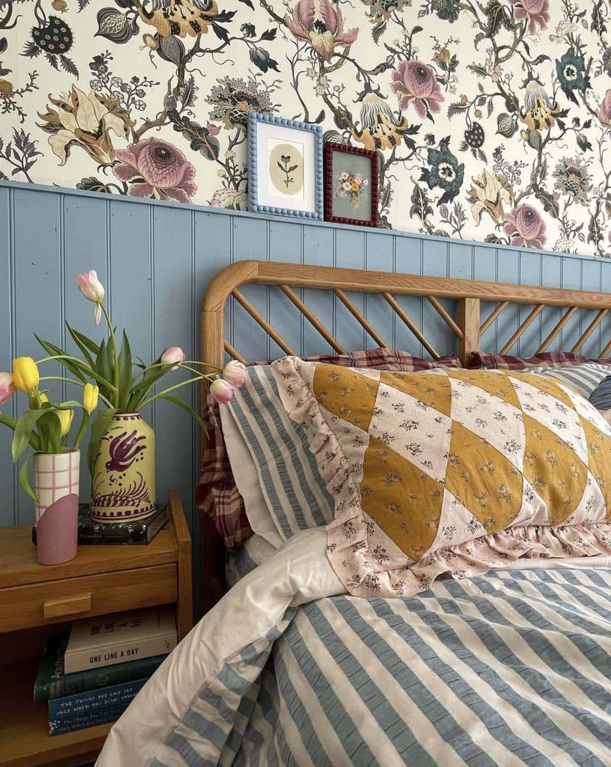 9:32 PMEclectic spring bedroom with bold floral wallpaper, blue wainscoting, rattan bed and patchwork quilt