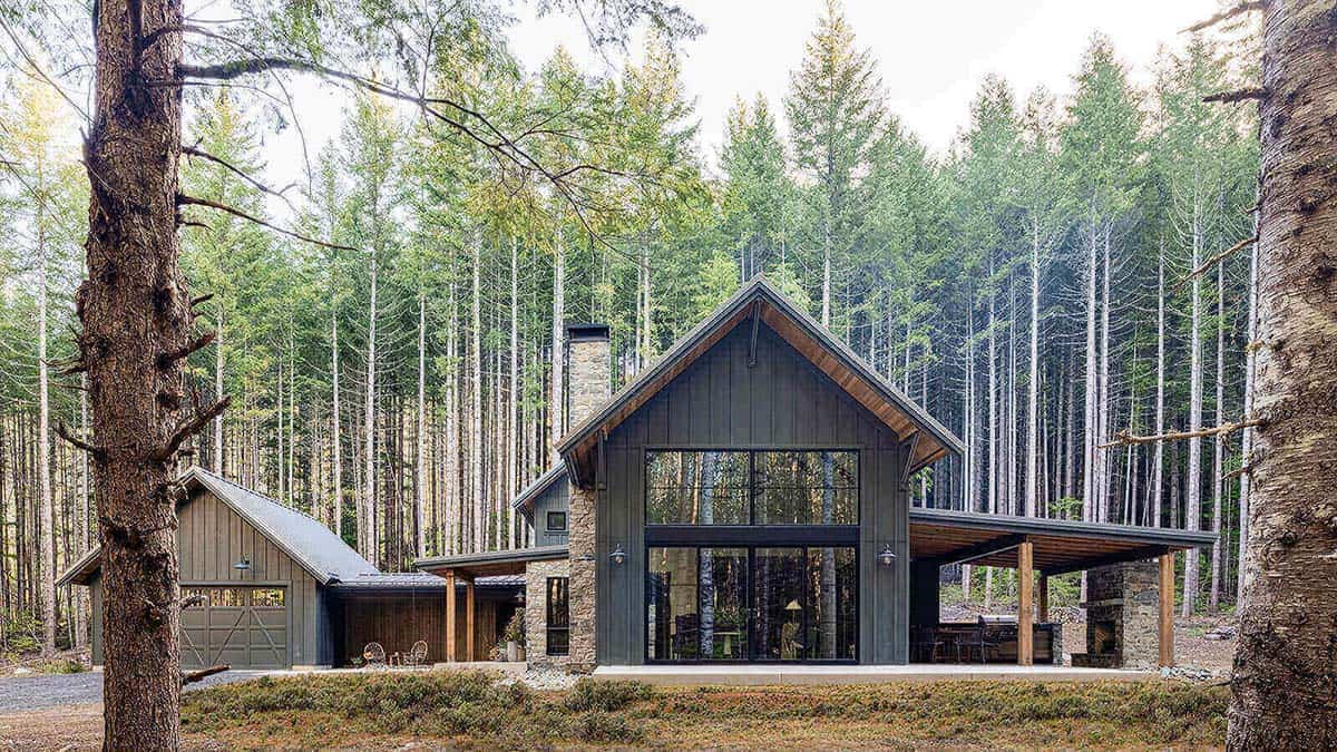 Exterior of alpine cabin nestled in pine forest with vaulted gable, stone chimney, and covered patio, Greenwater, Washington