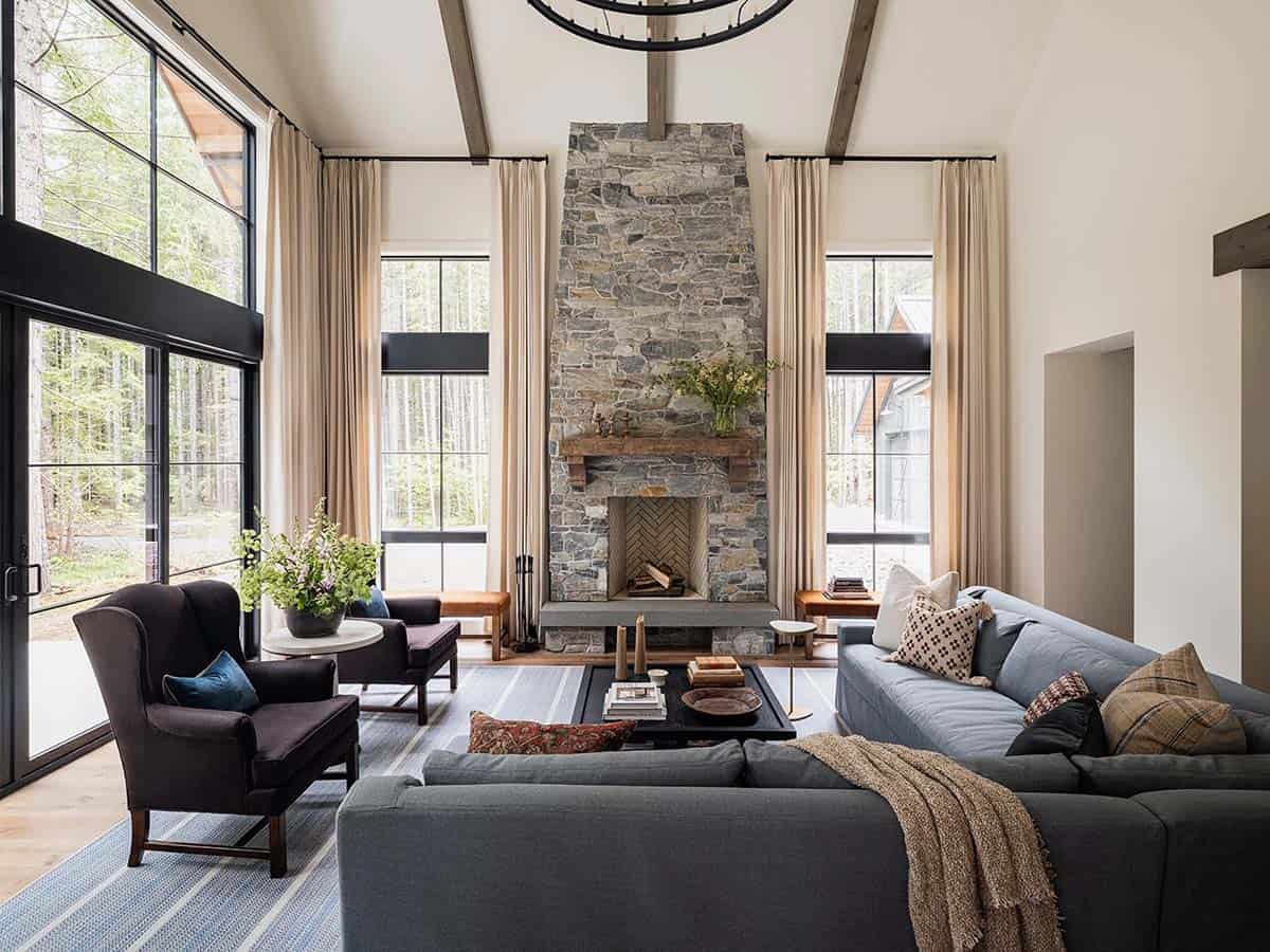 Open living room with stone fireplace, gray sectional sofa, wingback chairs, and panoramic forest views, Greenwater, Washington