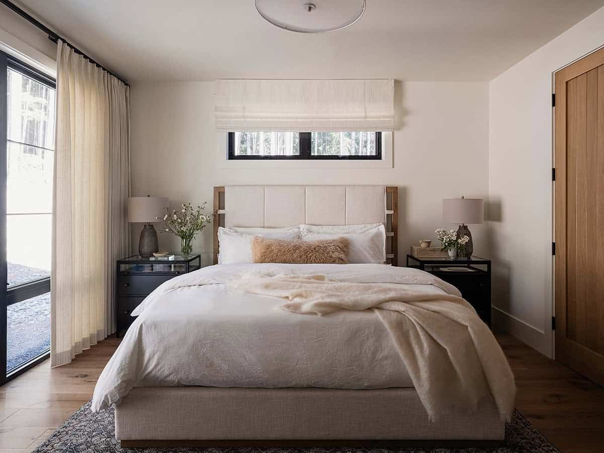 Primary bedroom with upholstered headboard, layered white bedding, forest views, and oak door, alpine cabin near Mt. Rainier
