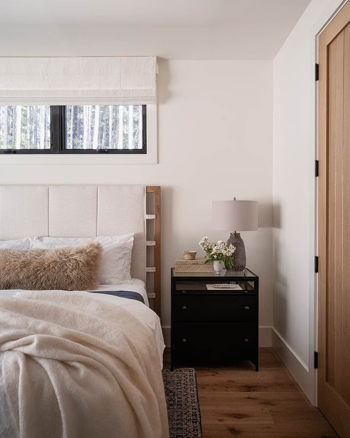 Primary bedroom detail with upholstered headboard, black nightstand, and forest views, alpine cabin near Mt. Rainier