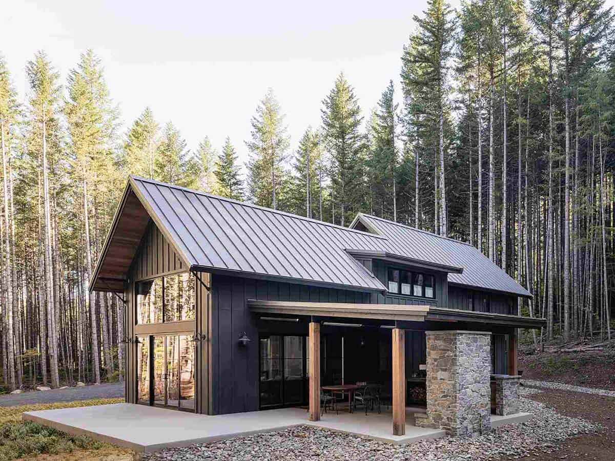 Rear exterior of alpine cabin with metal roof, covered patio, stone fireplace, and pine forest, Greenwater, Washington