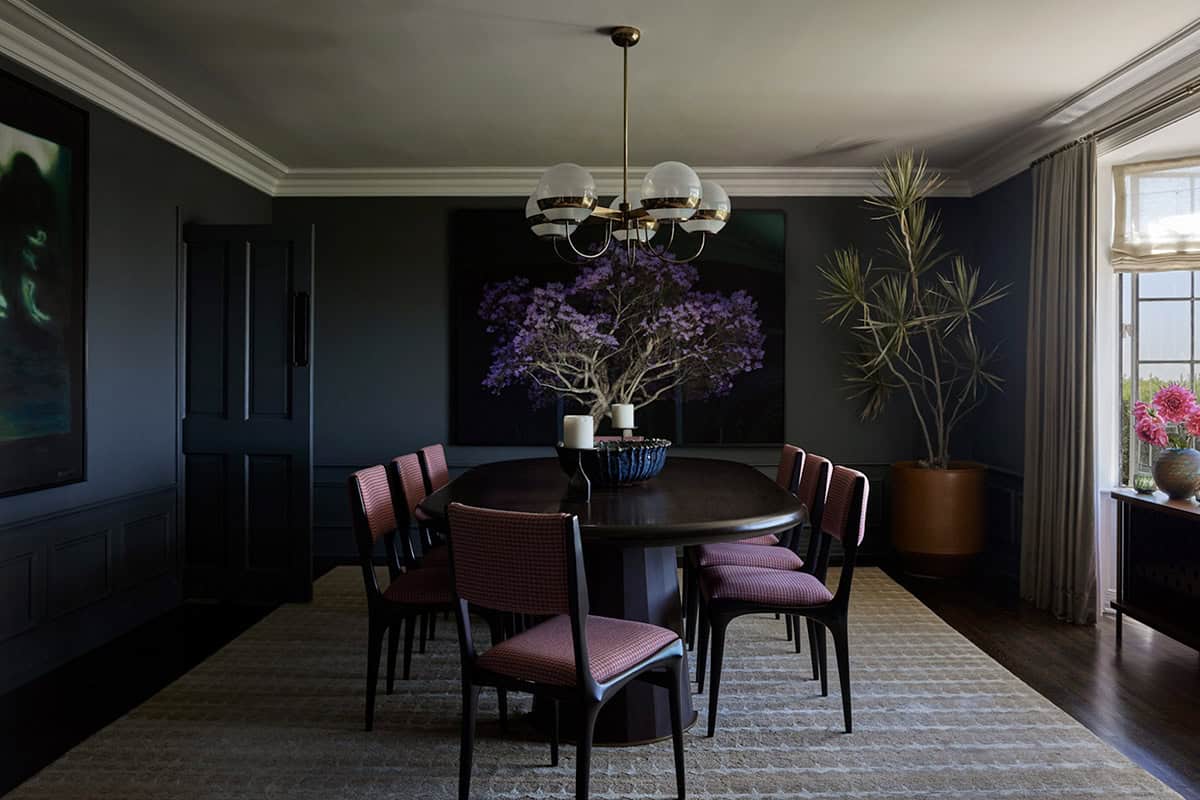 Dark dining room with oval table, pink houndstooth chairs, and globe chandelier, Los Feliz colonial revival home