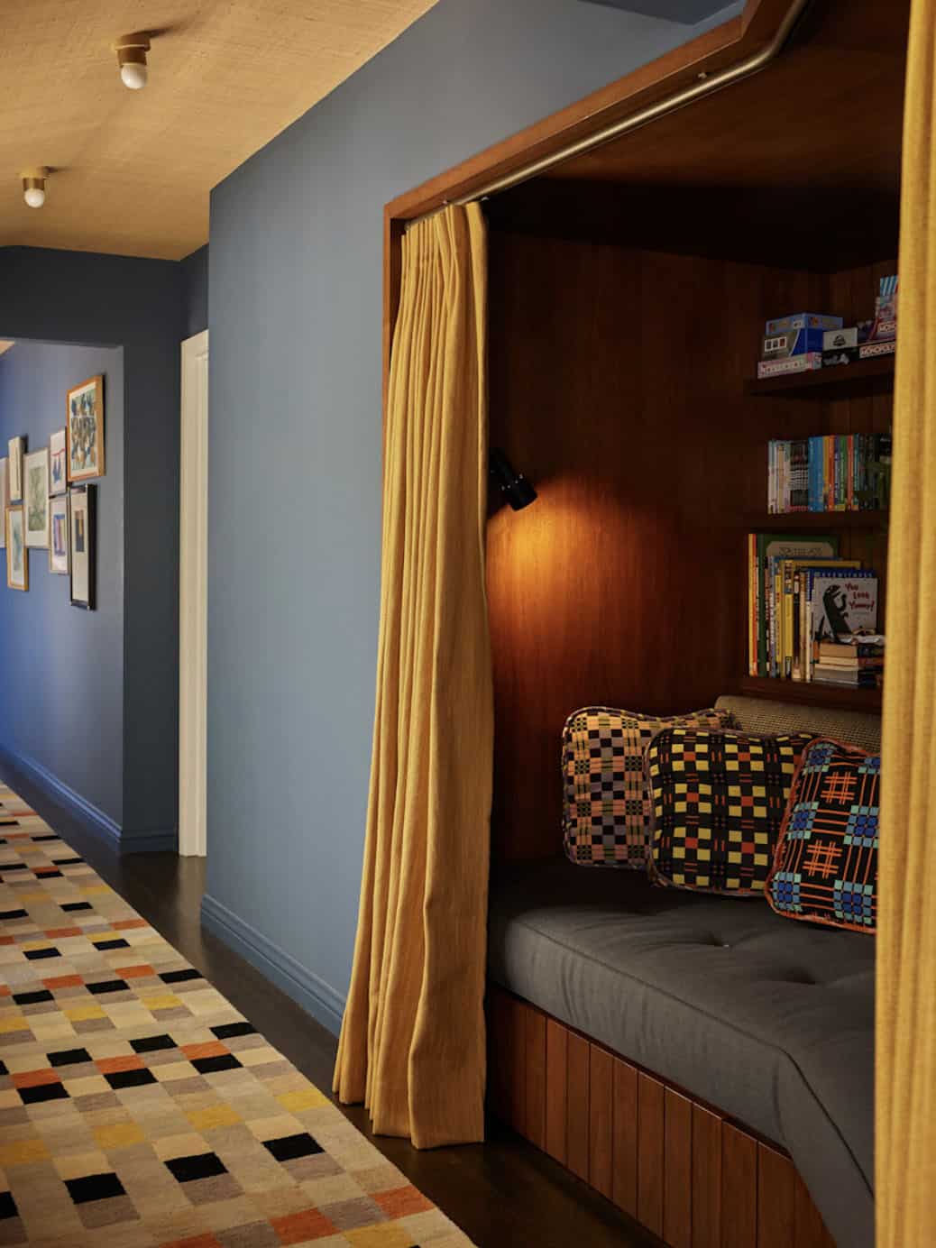 Hallway reading nook with wood paneling, yellow curtain, and colorful checker rug, Los Feliz colonial revival home