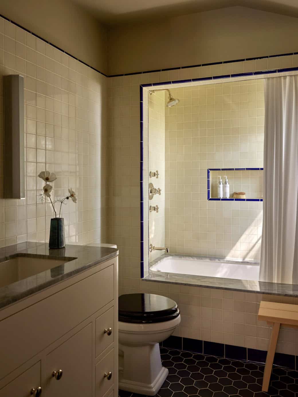 Bathroom with cream tile, cobalt blue trim, marble tub surround, and dark hexagon floor tile, Los Feliz home by Commune Design