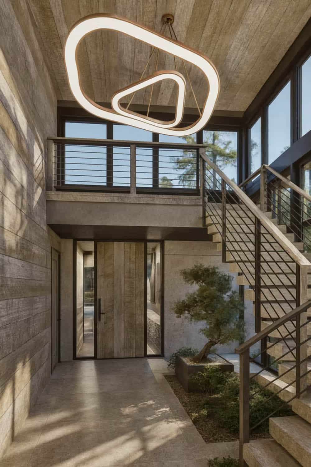 Contemporary home entryway with sculptural pendant light, wood pivot door, floating staircase, and indoor bonsai tree in Hudson Wisconsin
