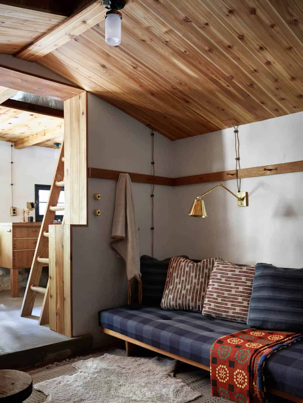 Living room with plaid daybed, brass wall sconce, and wood ladder to sleep loft