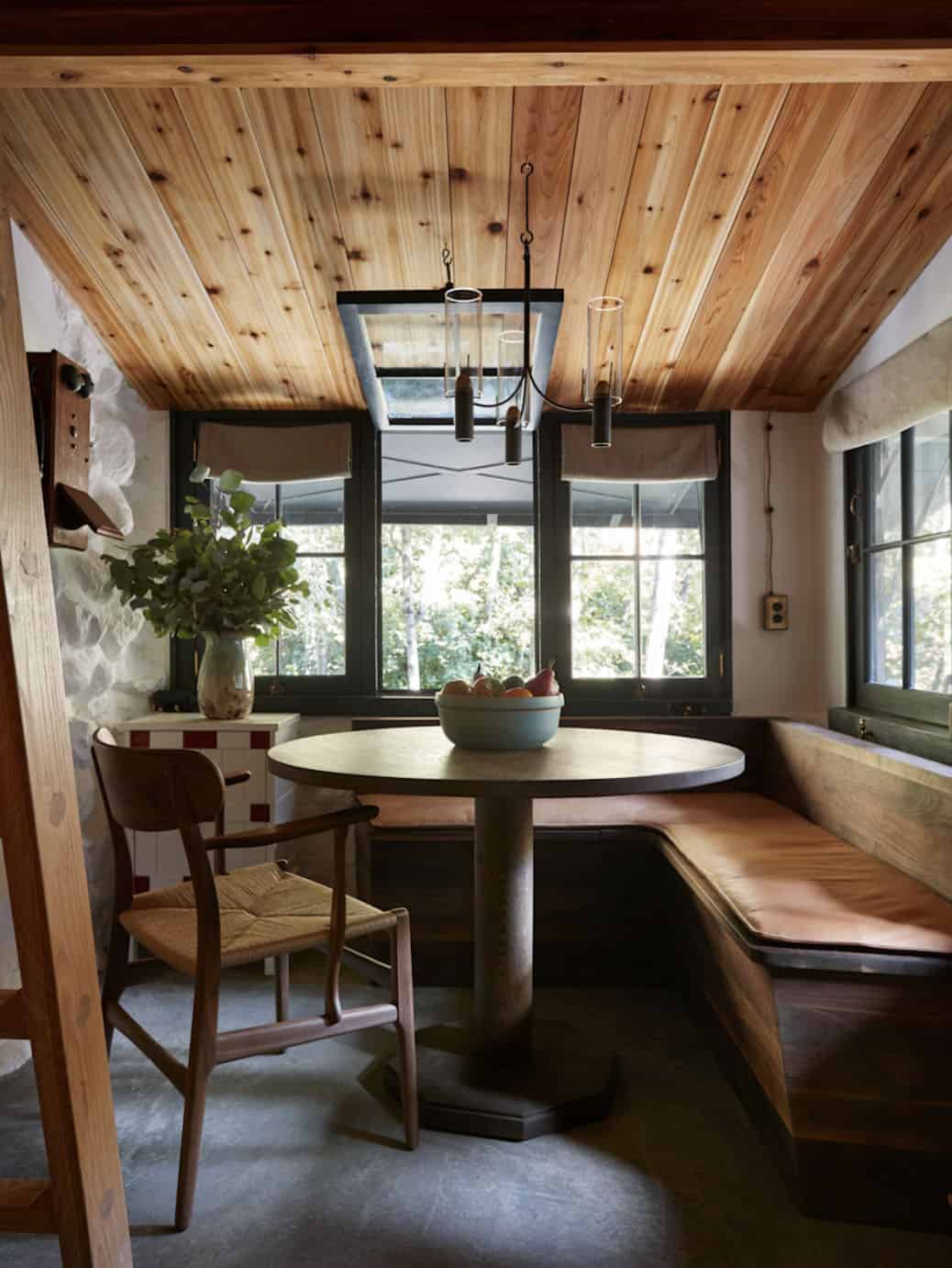 Dining nook with leather banquette, round pedestal table, and knotty pine ceiling