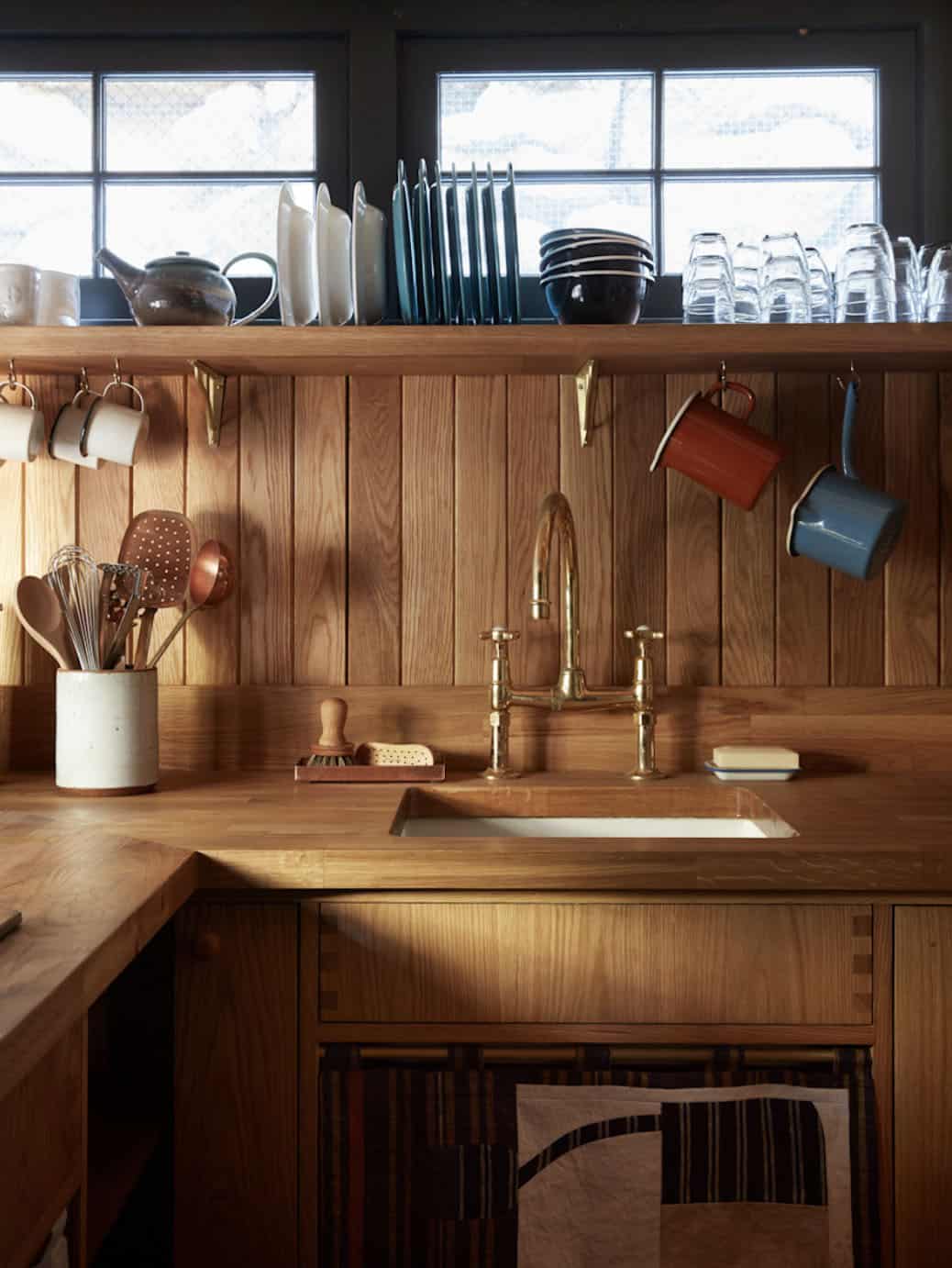 Kitchen detail with oak butcher block countertop, brass bridge faucet, and hanging mugs