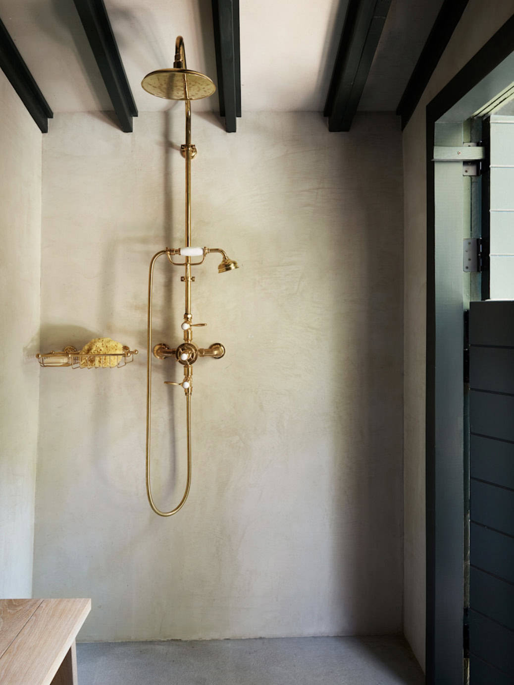 Outdoor shower with brass rainfall fixture and limewash walls