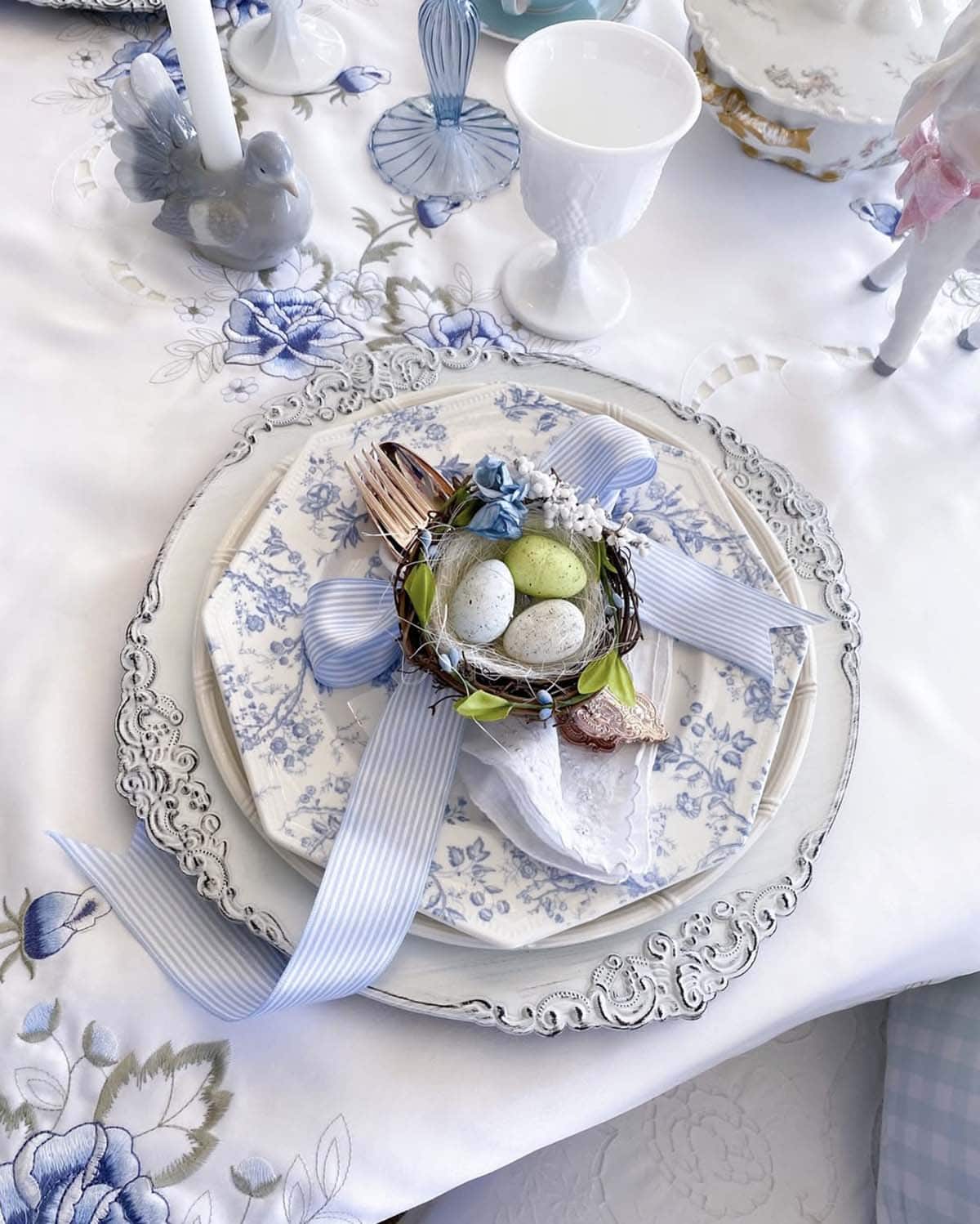 Blue and white Easter table place setting with bird's nest, speckled eggs, and striped ribbon on toile plates