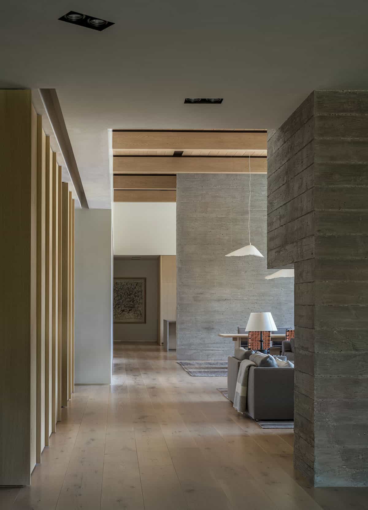 Interior hallway with board-formed concrete wall, oak slat partition, and view to living area