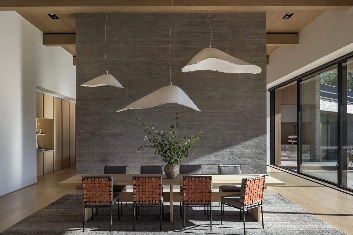 Dining room with wood table, woven leather chairs, and sculptural white pendant lights against concrete wall