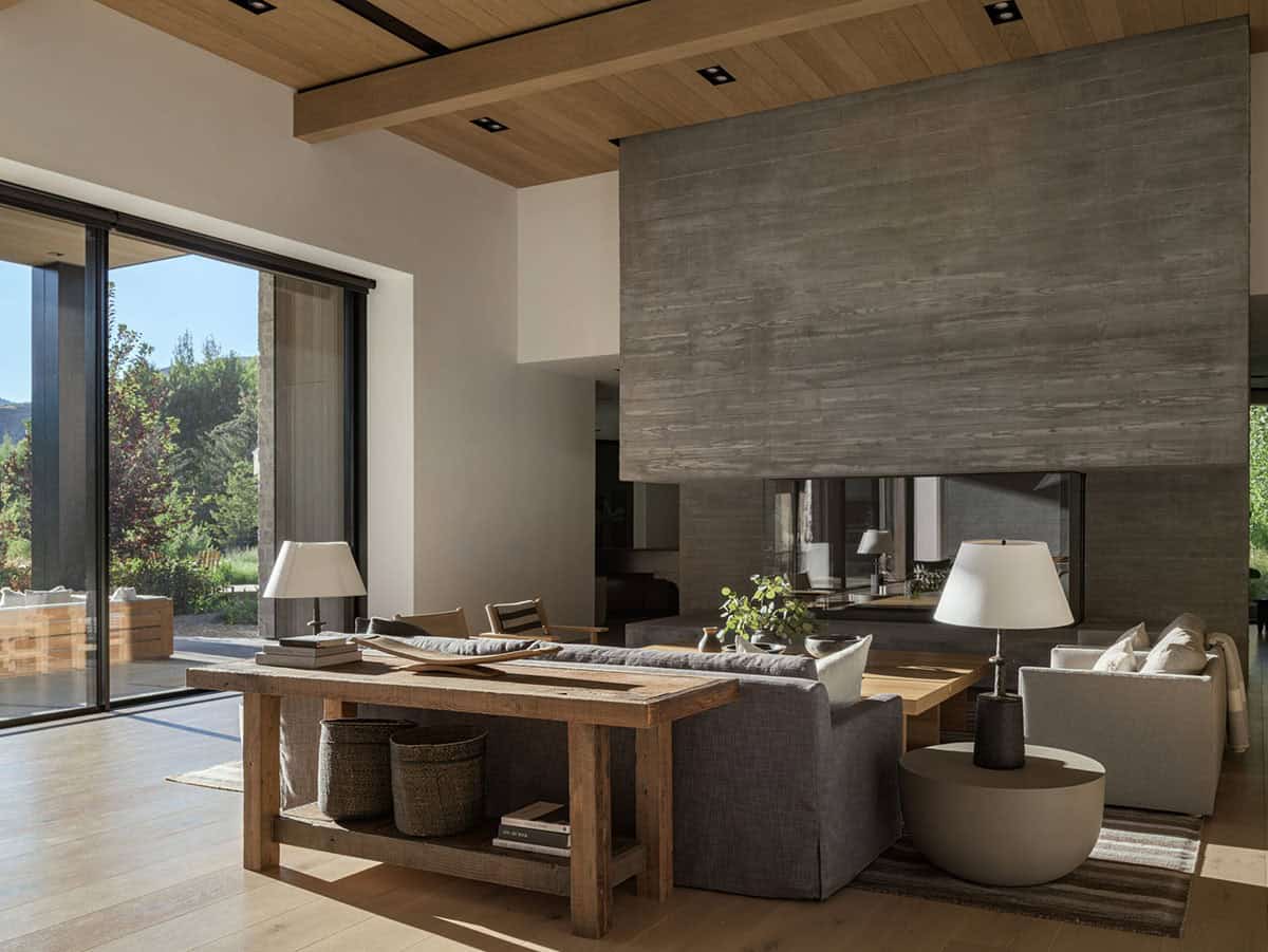 Open living room with double-sided board-formed concrete fireplace and sliding glass doors to garden