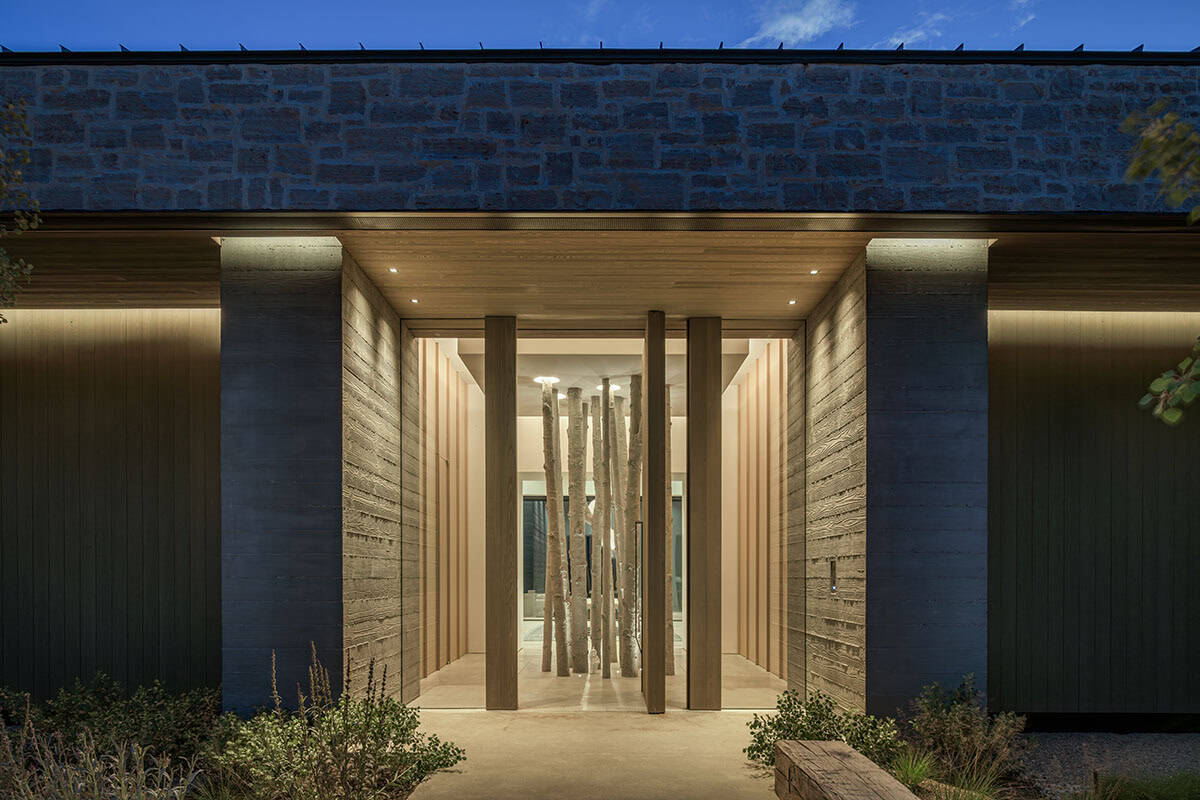 Illuminated entry portal at dusk revealing aspen trunk installation inside board-formed concrete foyer